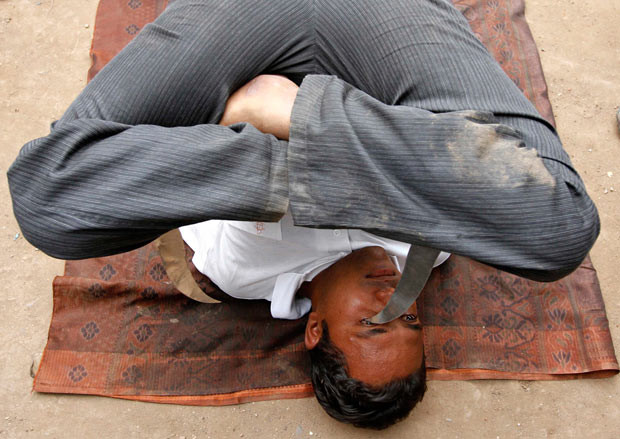A Hindu devotee applies kohl on his eyes with a knife held between his legs as he performs a stunt during a rehearsal for the 134th annual Rath Yatra, or chariot procession, in Ahmedabad, India
