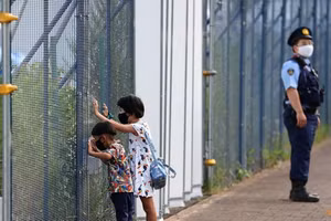 2 em nhỏ Nhật Bản đeo khẩu trang nhìn qua hàng rào của Công viên Thể thao Đô thị Aomi.