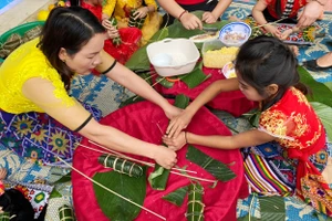 Cô giáo hướng dẫn học sinh tự tay gói bánh chưng trong hoạt động trải nghiệm Ngày Tết quê em.