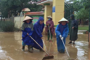 Giáo viên đẩy bùn ra khỏi trường học theo dòng nước lũ rút đi.