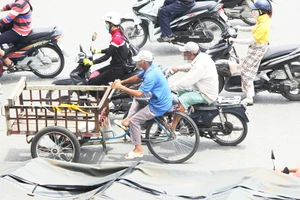 Người lái xe máy cũ vừa không đội mũ bảo hiểm vừa đẩy xe khác trên đường phố TP.HCM. Ảnh: HOÀNG GIANG