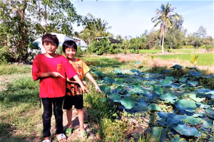 Em Nghị (áo đỏ) và em Nguyện chỉ vị trí bé gái bị rơi xuống ao sen.