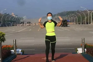 Người phụ nữ tập aerobics khi xe quân sự chạy sau lưng.