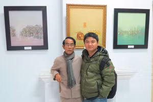 Họa sĩ Thân Văn Huy (người đeo kính) chụp hình lưu niệm tại phòng triển lãm của mình 