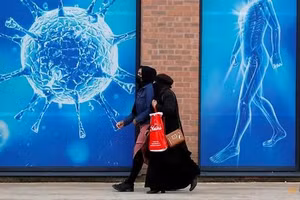 Người dân đi qua hình ảnh minh họa virus bên ngoài trung tâm khoa học khu vực ở Oldham, Vương quốc Anh, giữa đại dịch COVID-19.