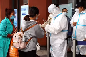 Nhân viên mặc đồ bảo hộ kiểm tra bằng chứng về kết quả xét nghiệm Covid-19 âm tính đối với du khách tại lối vào Ga xe lửa Tây Cáp Nhĩ Tân, Trung Quốc.