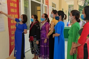 Bà Ngô Thị Lan - Hiệu trưởng Trường Tiểu học Pù Nhi, huyện Mường Lát, tỉnh Thanh Hóa (áo dài màu xanh đậm) đang cùng giáo viên nhà trường tìm hiểu danh sách các ứng cử viên tại điểm bầu cử.