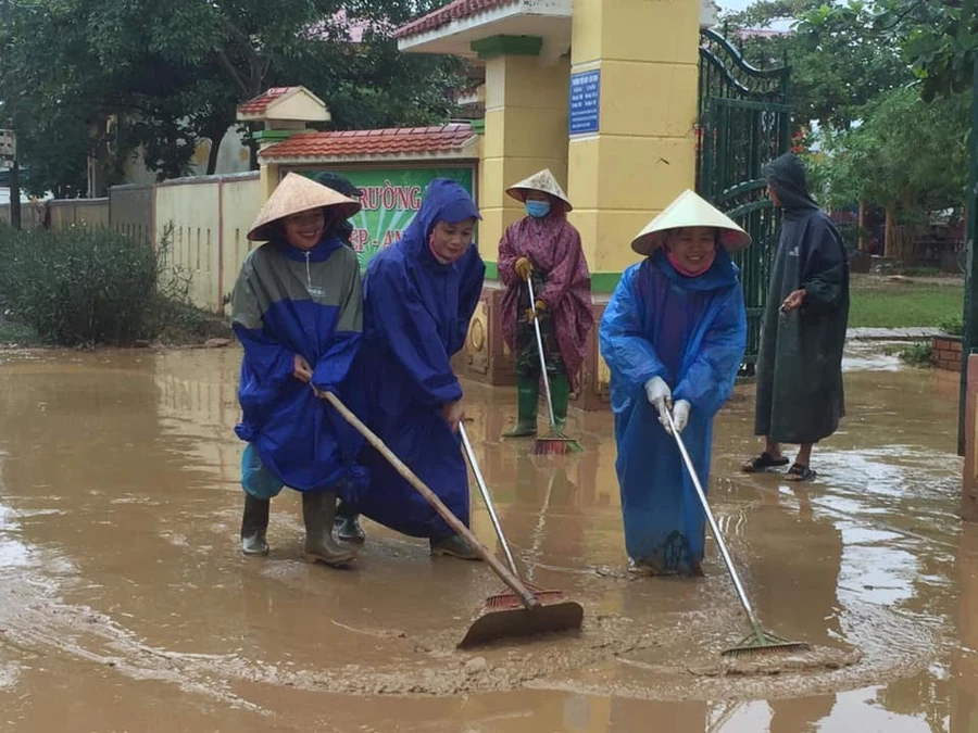 Giáo viên đẩy bùn ra khỏi trường học theo dòng nước lũ rút đi.