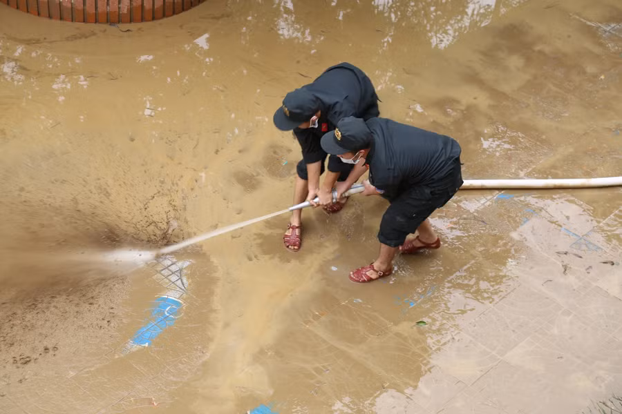 Dùng bơm cao áp để xịt bùn ra khỏi sân trường