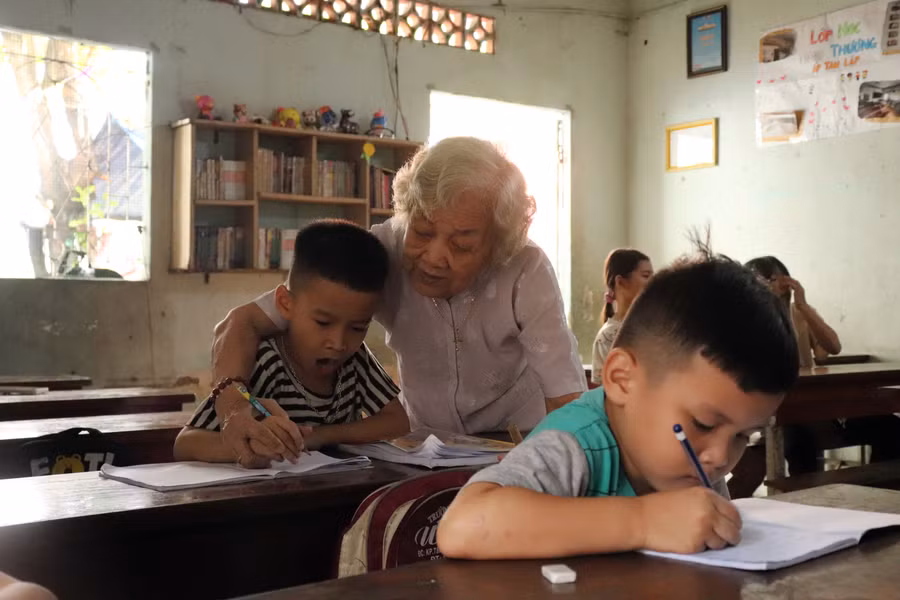 Bà Tư cầm tay dạy trẻ viết chữ. Ảnh: Bùi Vân Bà Tư cầm tay dạy trẻ viết chữ. Ảnh: Bùi Vân