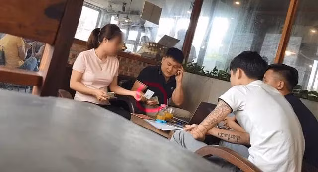 Đối tượng Ngọc Anh (nghe điện thoại) nhận làm hồ sơ, tiền của người có nhu cầu làm hộ chiếu tại quán cà phê, sau đó hướng dẫn đến làm nhanh tại một cửa duy nhất tại trụ sở Phòng Quản lý XNC, Công an Hà Nội trên phố Phạm Ngọc Thạch, Hà Nội. Ảnh: TPO.