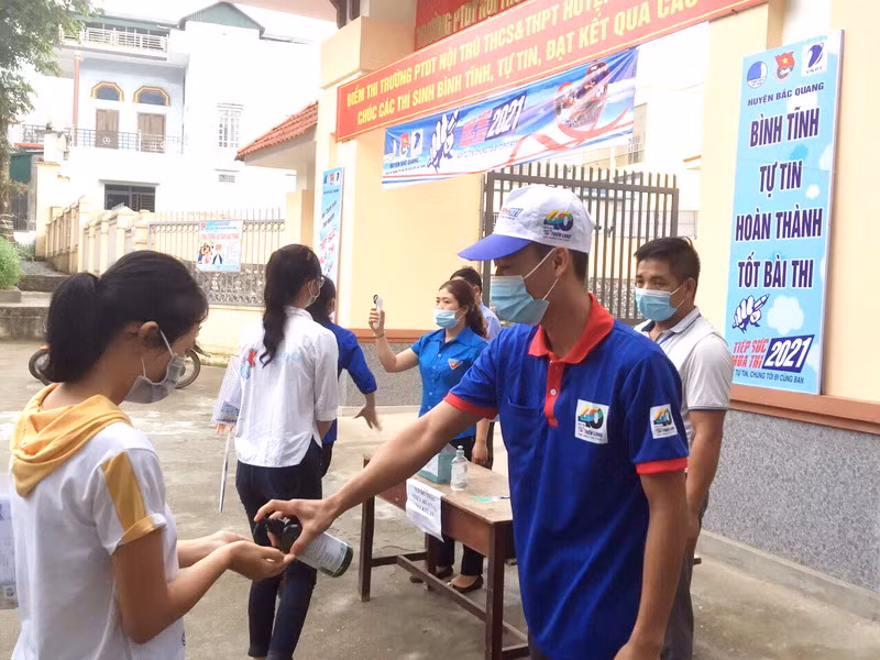 Thanh niên tình nguyện đo thân nhiệt và bơm dung dịch rửa tay sát khuẩn cho thí sinh. Ảnh: Bá Hải