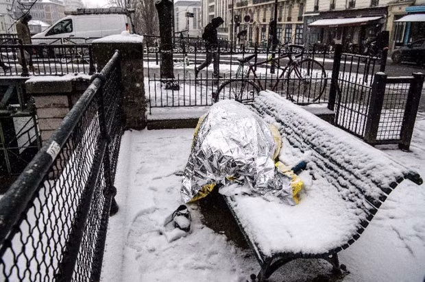 Người đàn ông đắp chăn ngủ trên băng ghế phủ đầy tuyết ở Paris. Ảnh: AFP