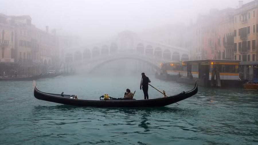Một chiếc thuyền đi qua sông Venice (Italy) khi kênh đào Grand và cầu Rialto bị che khuất trong sương mù.