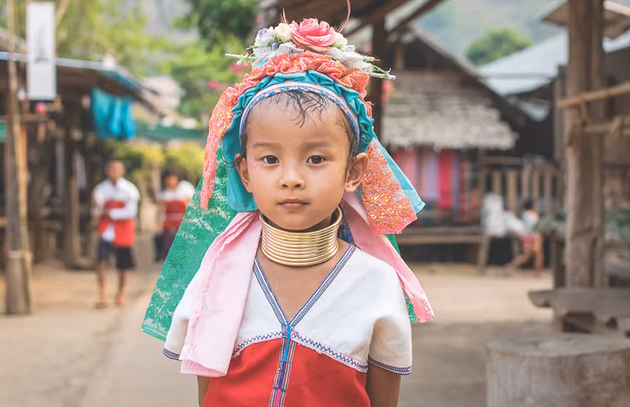 Một cô bé đeo vòng cổ và đội hoa trên đầu. Một giả thuyết cho rằng, đeo vòng cổ giúp bảo vệ phụ nữ của bộ lạc khỏi các cuộc tấn công của hổ khi cổ của họ được che kín.