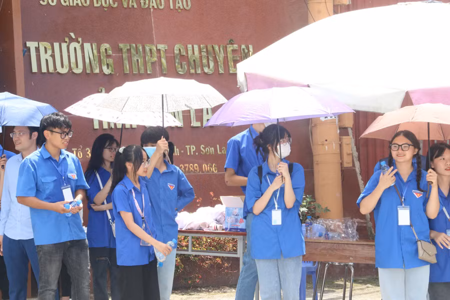 Các thanh niên tình nguyện đưng che ô hỗ trợ nước và bút cho các thí sinh dự thi tốt nghiệp THPT năm 2022.