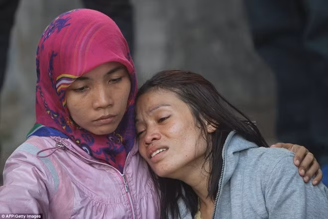 Hai người phụ nữ an ủi nhau tại hiện trường tai nạn. Đến 19h ngày 30/6, một nguồn tin cho biết họ đã thu hồi 55 thi thể. Ảnh: AFP