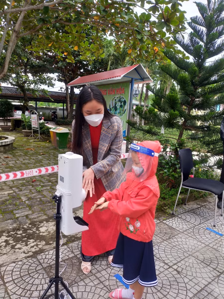 Một học sinh lớp Một được phụ huynh trang bị mũ ngăn giọt bắn để sử dụng trước khi vào giờ học chính thức