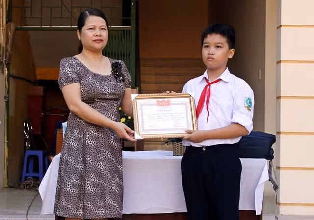 Hiệu trưởng trường THCS Tây Mỗ, cô Đỗ Thị Ánh Tuyết trao giấy khen cho em Hưng