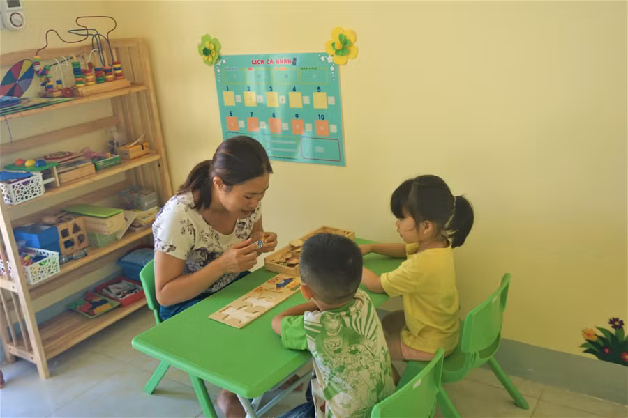 Giáo viên hướng dẫn học sinh ghép hình và tập đếm trong giờ can thiệp nhóm.