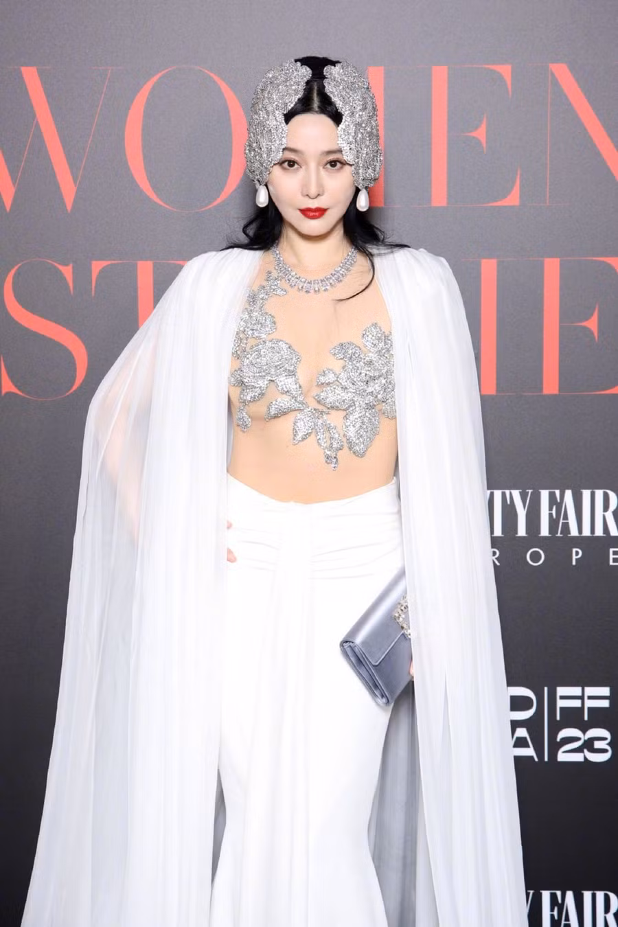 Được biết, bộ trang phục này tới từ thương hiệu Miss Sohee, với phần thân trên xuyên thấu, vòng một được che lấp khéo léo bởi những bông hoa thêu ánh bạc táo bạo. Váy và áo choàng trắng tinh khôi, thanh lịch, phần tà dài quét đất.
