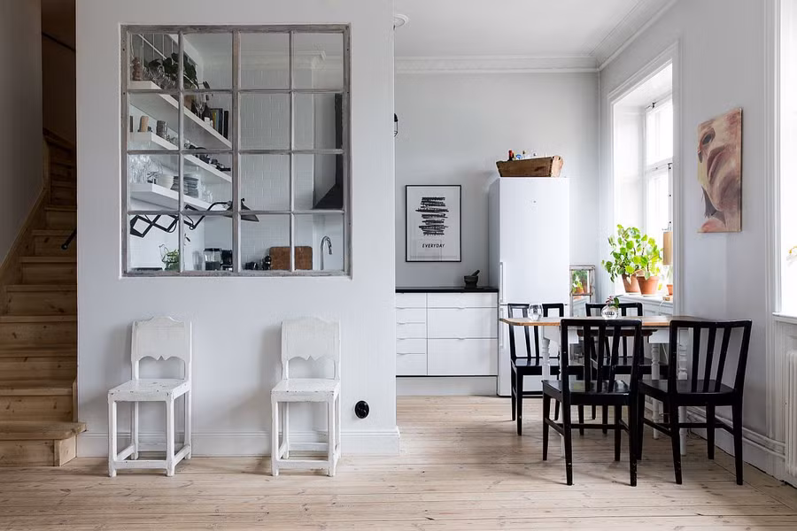 Góc bếp khéo léo lựa chọn màu trắng với hệ tủ bếp dưới kết hợp kệ trắng phía trên. Không gian càng thêm nổi bật khi có thêm bộ bàn ghế nhỏ xinh màu đen tương phản ở gần khung cửa sổ.