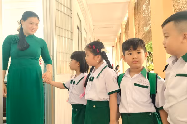 Học sinh được giáo viên chào đón trước cửa lớp.