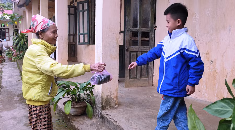 Bà đưa cơm cho cháu ăn trưa tại lớp ở điểm trường Tân Sơn - Trường Tiểu học Thanh Xuân. Ảnh: TL.