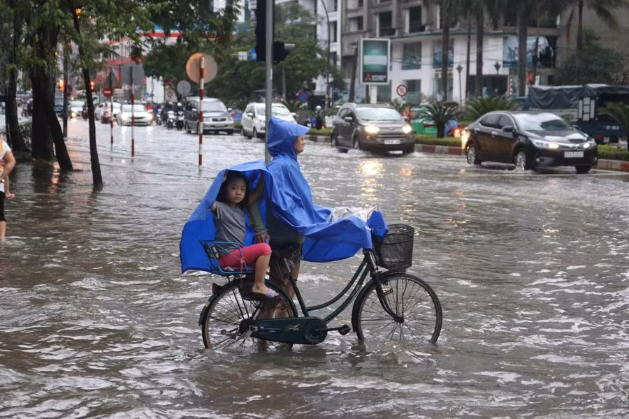 Bà chở cháu đi học về bằng xe đạp đứng trước tuyến phố bị ngập