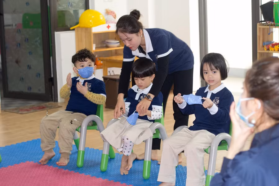 Cô giáo Trường Mầm non Rainbow đeo khẩu trang cho các bé