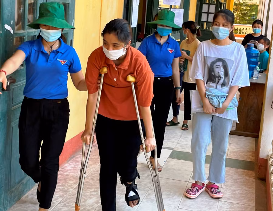 Một thí sinh nữ được lực lượng tình nguyện hỗ trợ đến phòng thi do bị thương ở chân.